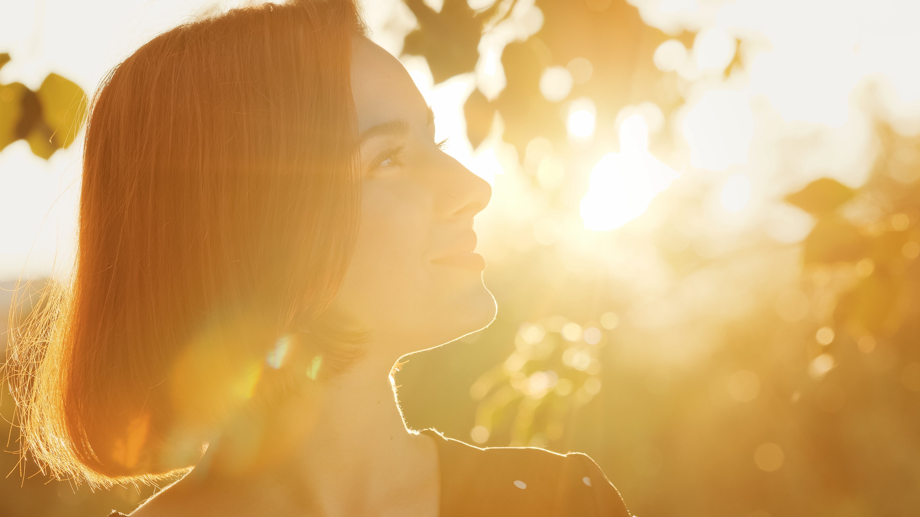 Femme qui sourait de profil dans la nature et un soleil couchant en fond